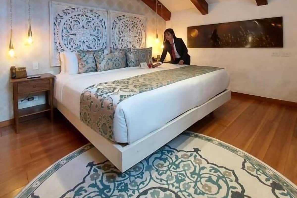 A bedroom with a large bed, wooden beams, a decorative headboard, a nightstand, and a patterned rug.