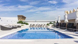 Ein Pool auf dem Dach mit Liegestühlen und Sonnenschirmen, ein klarer Himmel und ein Gebäude im Hintergrund.