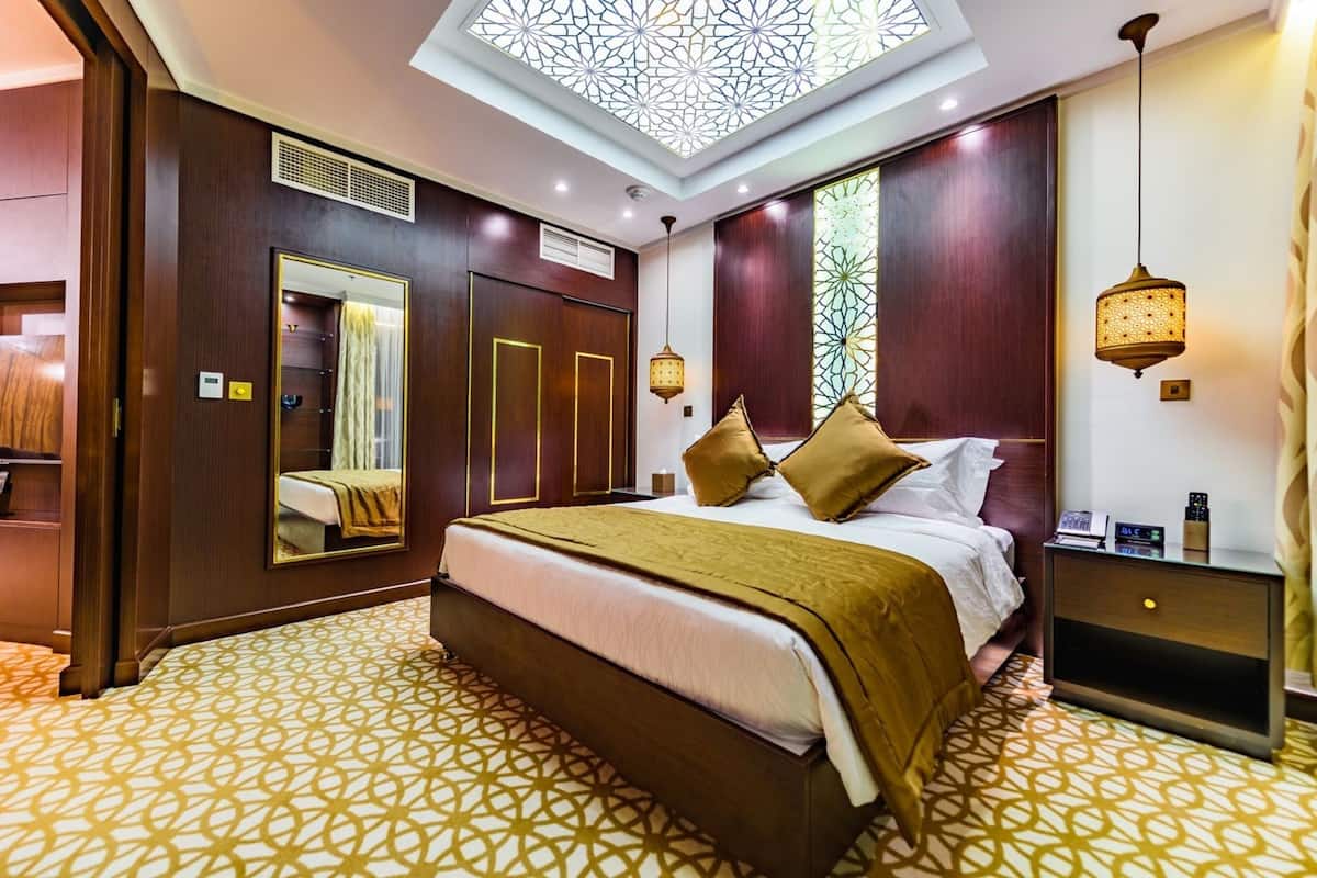 A hotel room with a large bed, a bedside table, a mirror, a wardrobe, and a skylight.