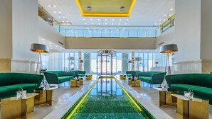 Eine geräumige Lobby mit einem zentralen Pool mit Glasabdeckung, grünen Sofas und modernen Leuchten.