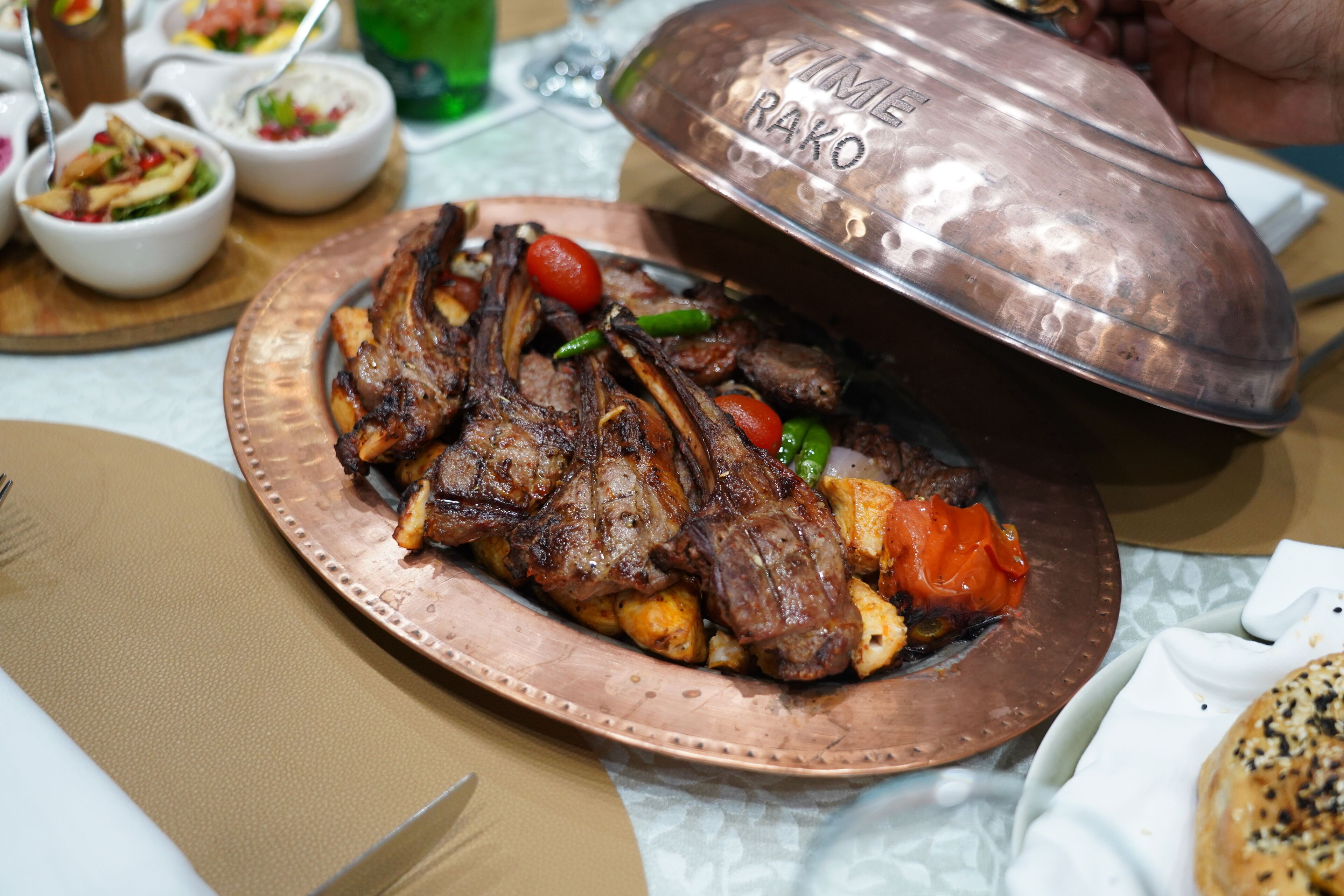 A copper pot labeled "TIME RAKO" containing grilled meat and vegetables on a table.