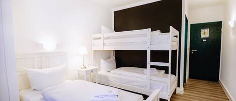 Una habitación con una cama litera, una mesita de noche con lámpara y una puerta de marco verde.