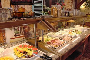 Un bufé con diversos platillos, entre ellos frutas, carnes y quesos.