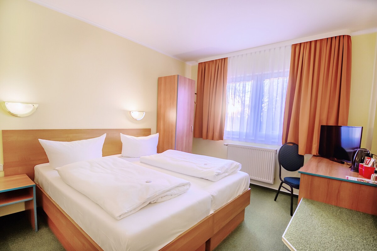 Una habitación de hotel con dos camas, un escritorio con computadora, una silla y un televisor.