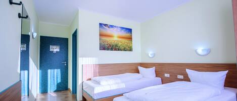 Habitación de hotel con dos camas individuales, cabecera de madera, un cuadro de un atardecer y un escritorio de madera.