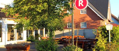 A hotel with a red 'R' sign indicating restricted parking, surrounded by greenery and outdoor seating.
