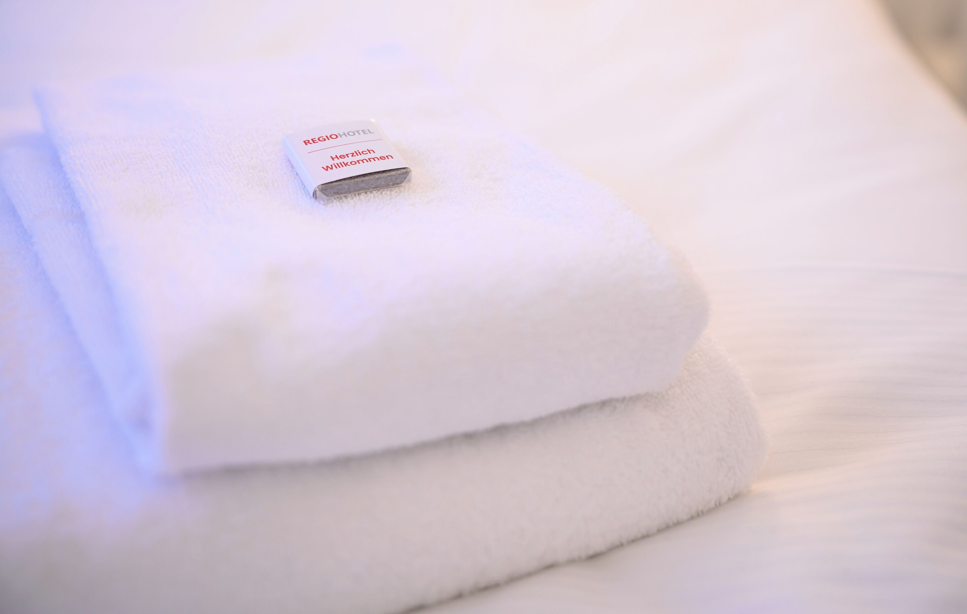 A neatly folded white towel with a tag that reads "REGENCY HOTEL Willkommen".
