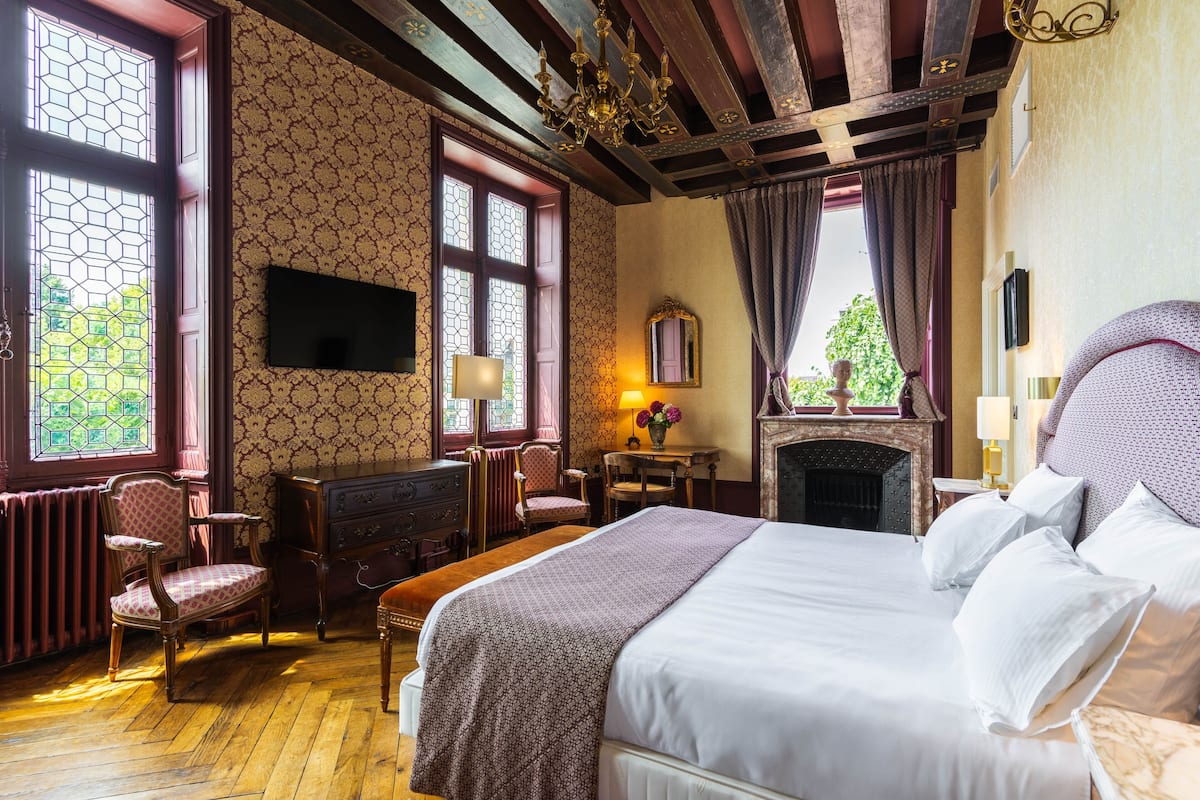 A traditional room with a large bed, wooden furniture, a fireplace, and large windows.