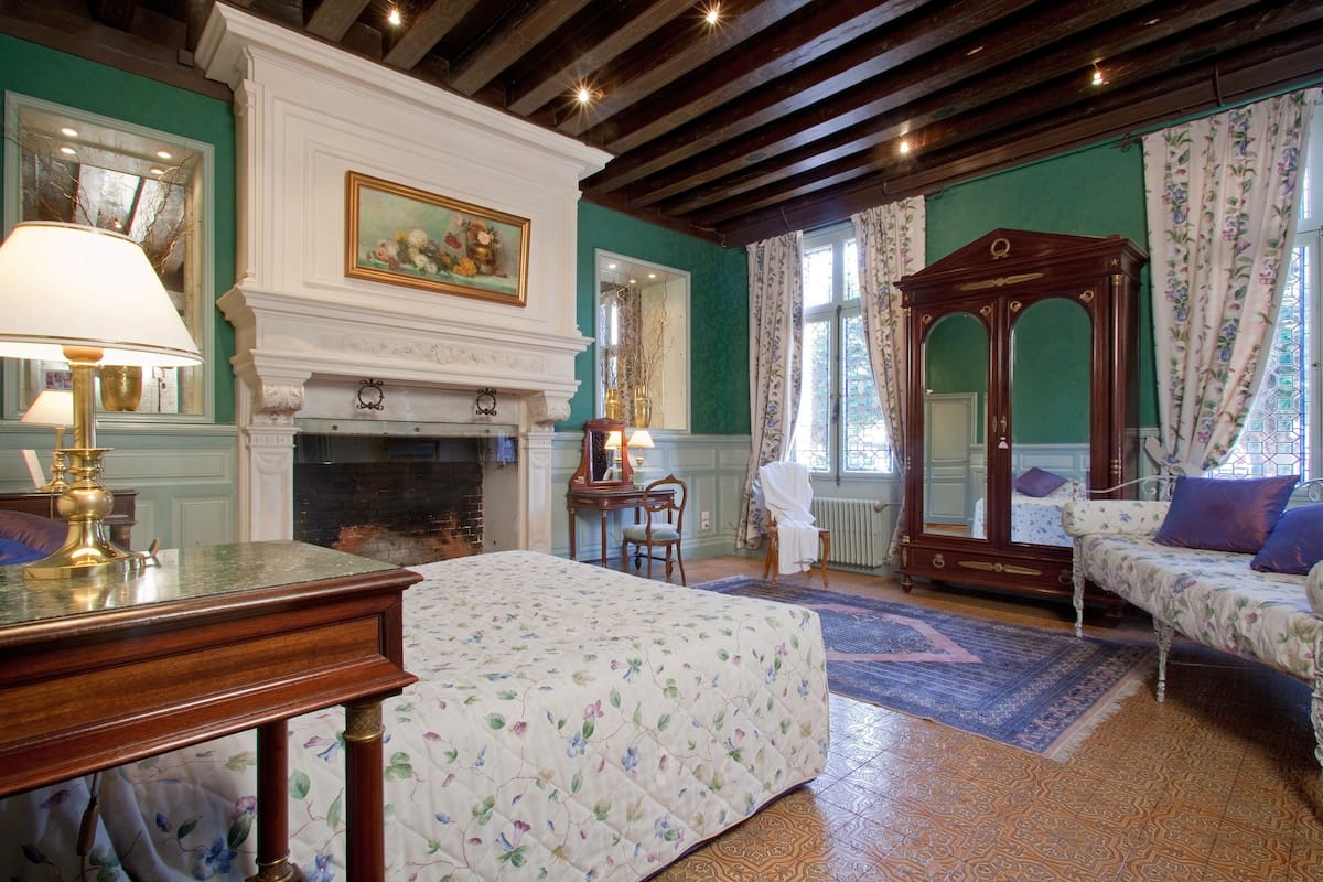 A room with a fireplace, a bed, a mirror, and a table with a lamp.