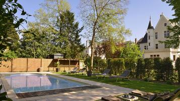 Una piscina con sillas de descanso, una valla de madera y un edificio grande con una torre al fondo.