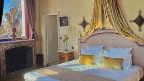 A spacious bedroom with a large bed, a chandelier, a fireplace, and a view of the outdoors. - Le Manoir Saint Thomas (Amboise)