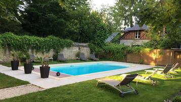 A rectangular swimming pool with a tiled deck, surrounded by a well-maintained lawn and potted plants.