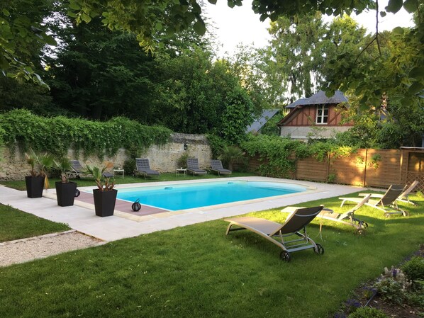 A rectangular swimming pool with a tiled deck, surrounded by a well-maintained lawn and potted plants.