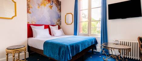 A bedroom with a bed, a blue carpet, a painting on the wall, a window with curtains, a radiator, and a television on the wall.