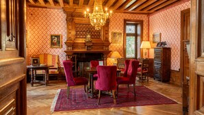 A room with a wooden ceiling, a chandelier, a fireplace, and red patterned wallpaper. - Le Manoir Saint Thomas (Amboise)