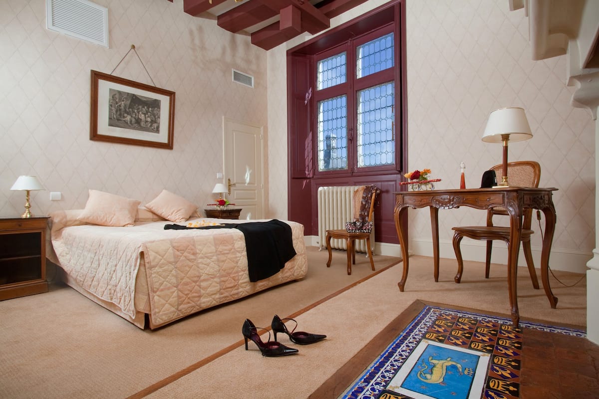 A bedroom with a bed, bedside tables, a chair, a table, and a window.