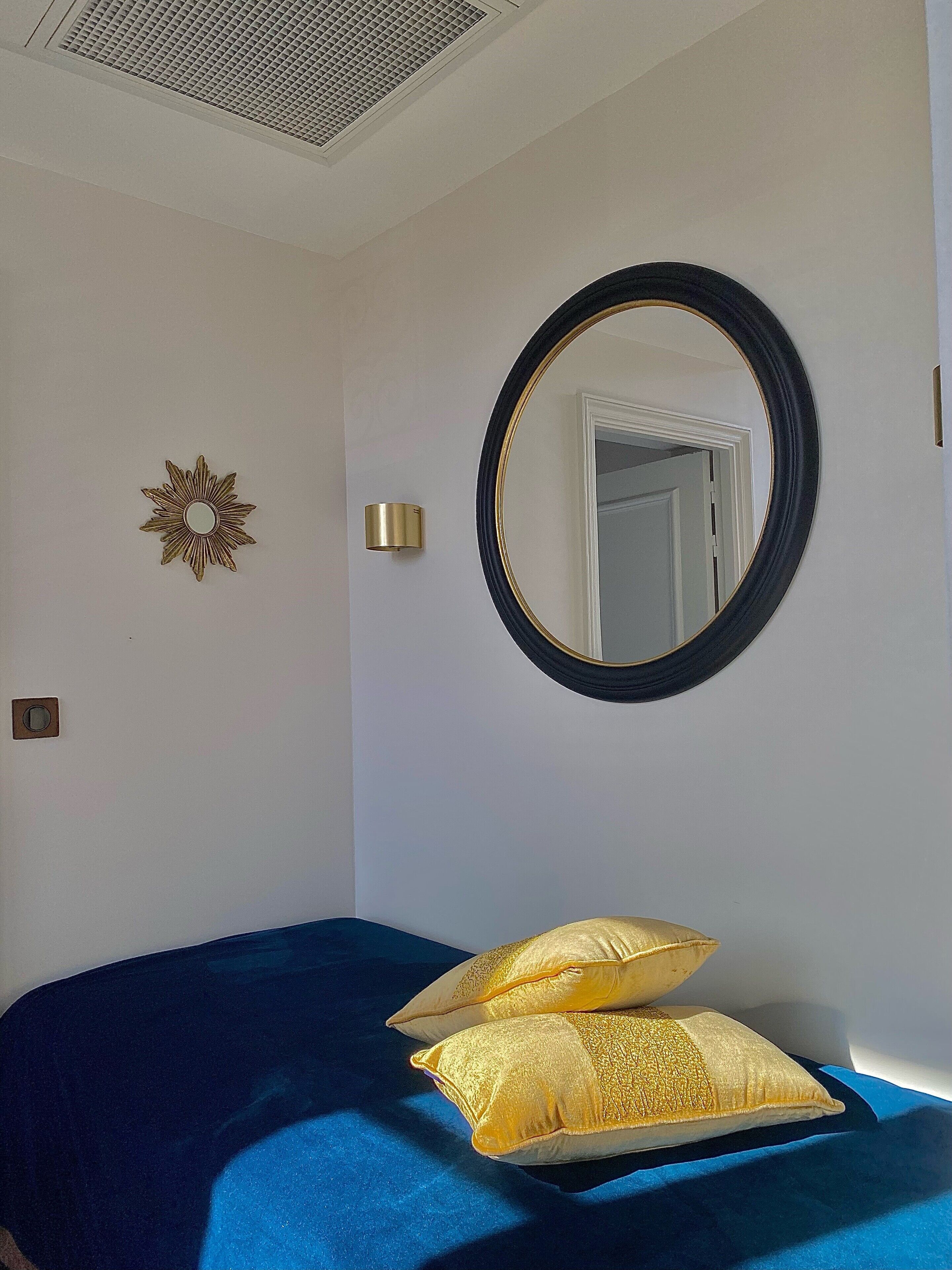Un dormitorio con una cama, un espejo redondo, un aplique de pared y una estrella decorativa en la pared.