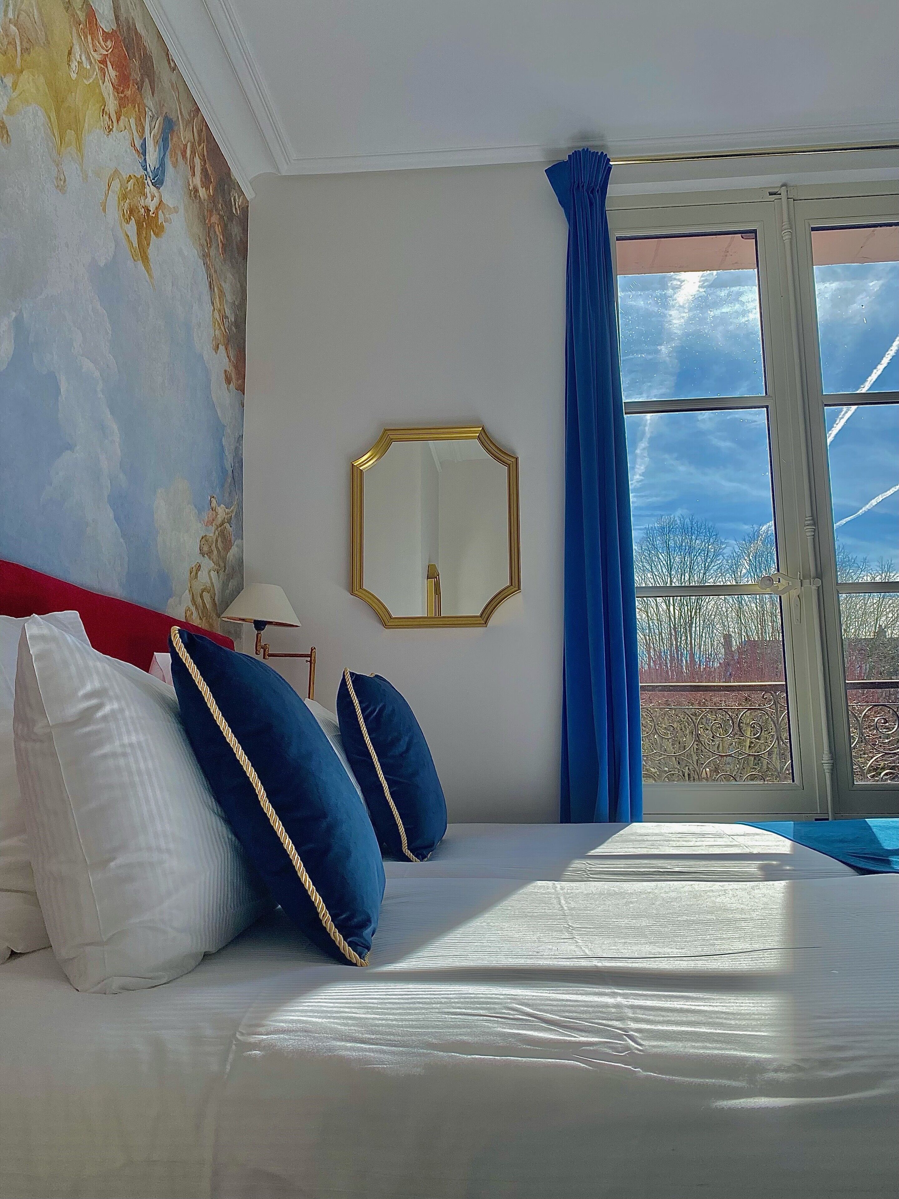 A hotel room with a bed, a large mirror, and a view of the sky through a window.