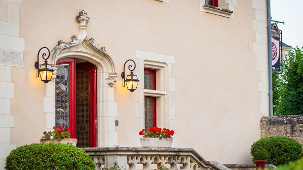 A building with a red door, two wall-mounted lights, and a small balcony with potted plants. - Le Manoir Saint Thomas (Amboise)
