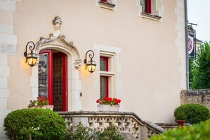 A building with a red door, two wall-mounted lights, and a small balcony with potted plants.
