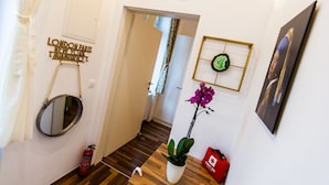 A hallway with a mirror, a plant, a fire extinguisher, a red bag, and a framed picture on the wall. - Cosy 2 bedroom Apartment (Vienna)