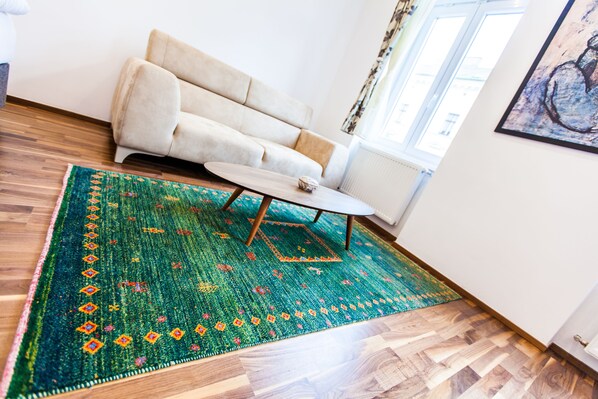 A room with a beige sofa, a wooden floor, and a green patterned rug.