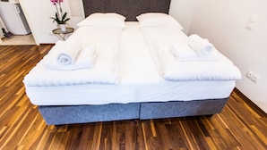 A double bed with white linens and towels, a grey headboard, and a wooden floor. - Cosy 2 bedroom Apartment (Vienna)