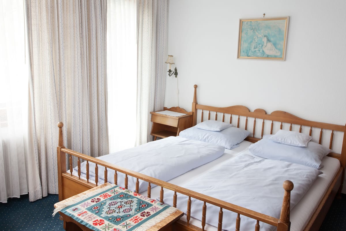 Cama bem arrumada com lençóis brancos, cabeceira de madeira e uma pequena mesa de cabeceira com abajur.