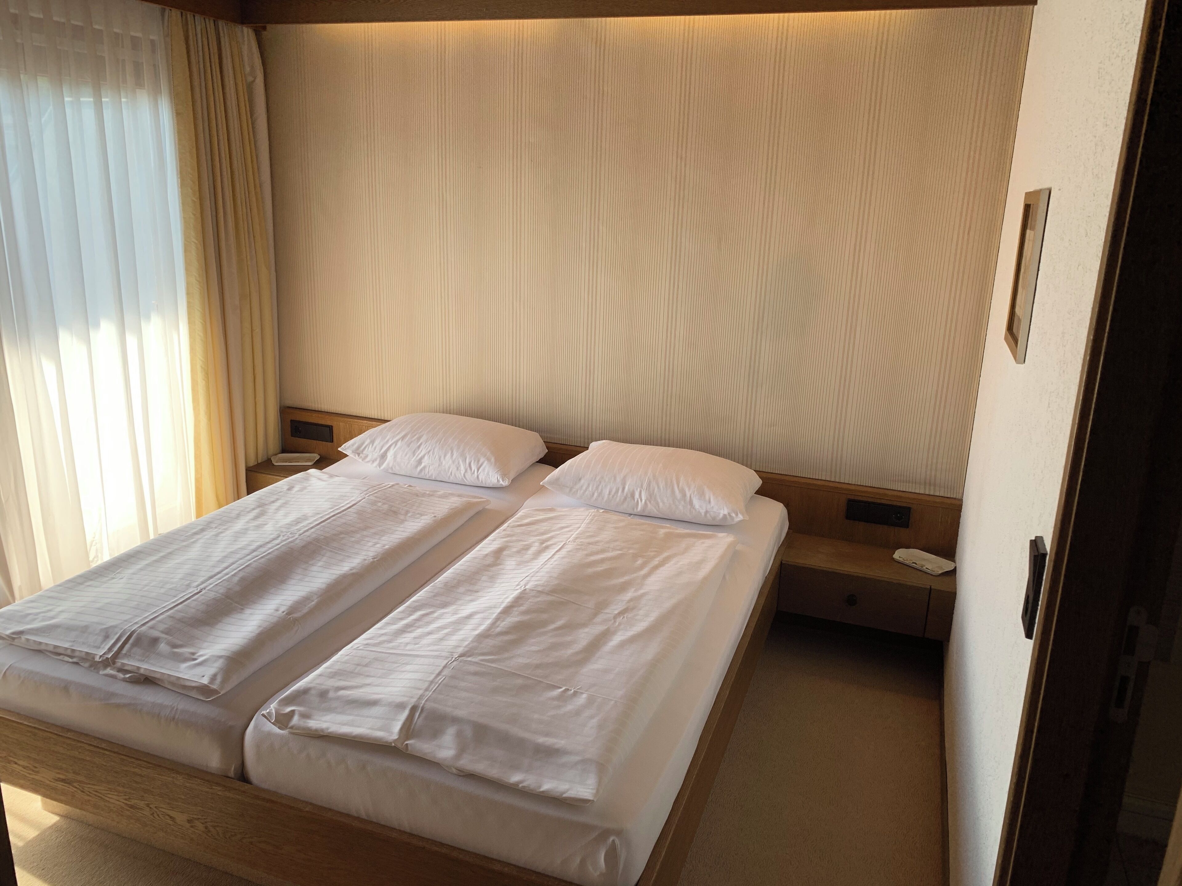 A double bed with white linens, a wooden headboard, and a bedside table with a lamp.