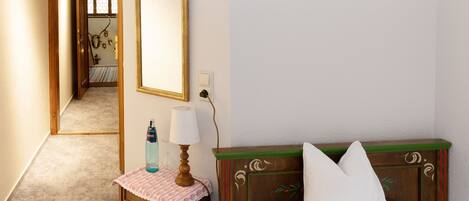 A hotel room with a bed, a bedside table with a lamp, a mirror, and a small table with a bottle.