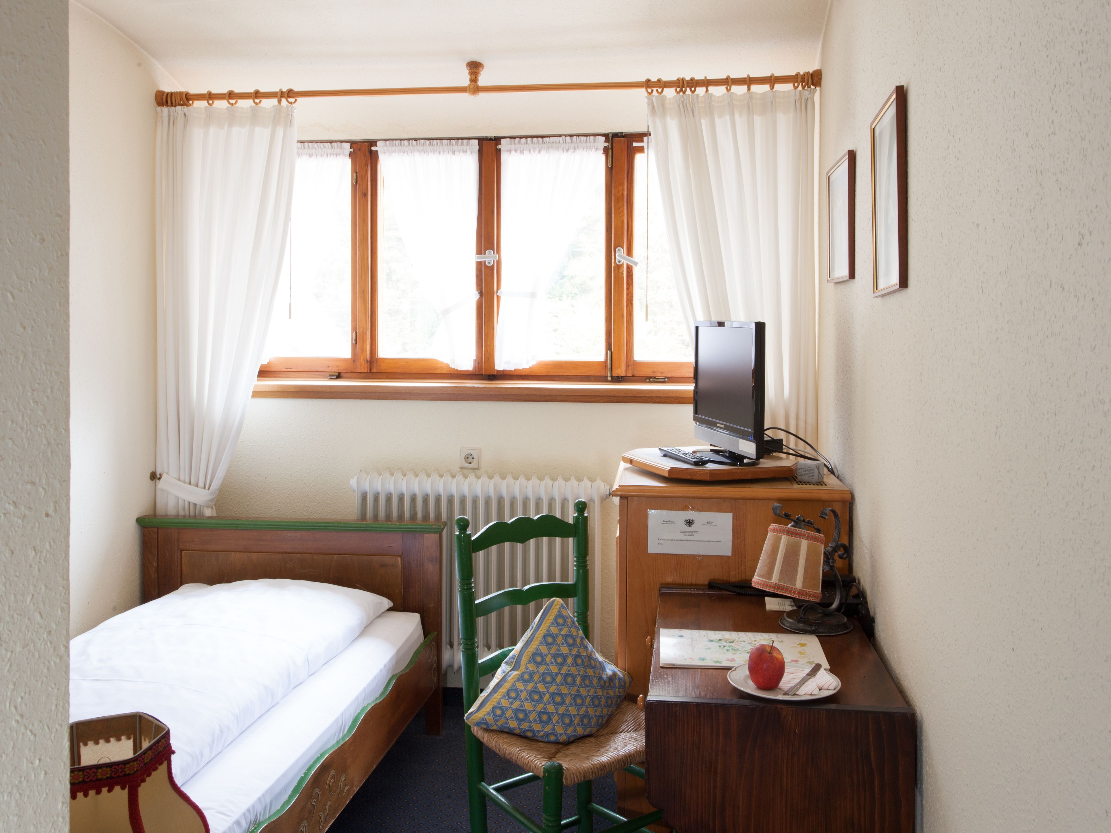 A room with a bed, a desk with a computer, a chair, and a window with curtains.