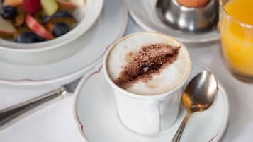 Ein Frühstückstisch mit einer Tasse Kaffee, Kakao, einer Fruchtschale, einem gekochten Ei und einem Glas Orangensaft.