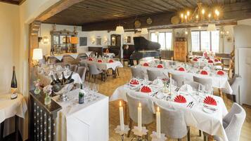 Un comedor con varias mesas dispuestas para una comida, con manteles blancos, velas y servilletas rojas.