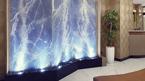 A modern lobby with a marble wall, a reception desk, a potted plant, and hanging pendant lights. - Artezen Hotel (New York)
