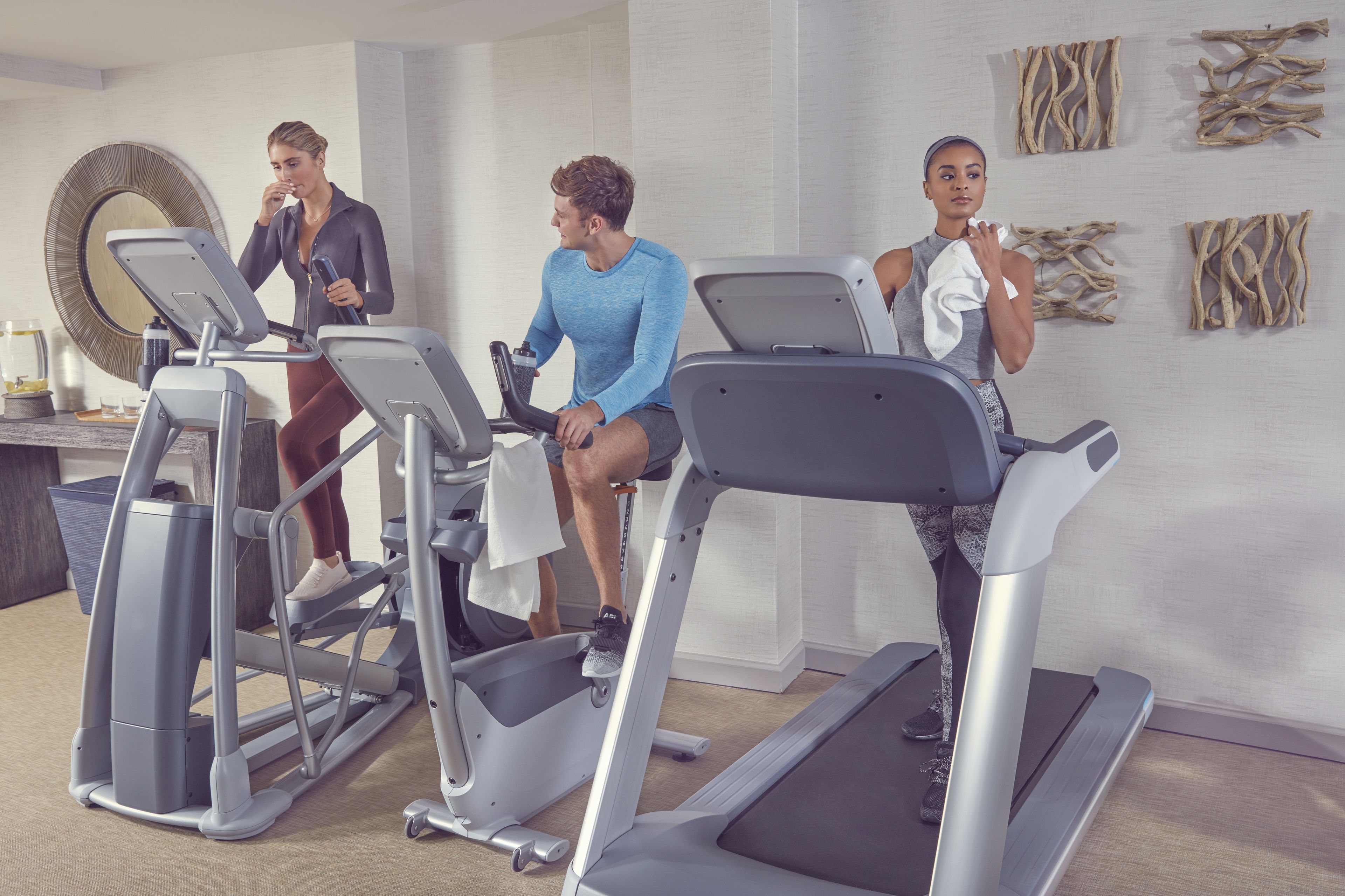 Three people using treadmills in a modern room with a large mirror and abstract wall art.