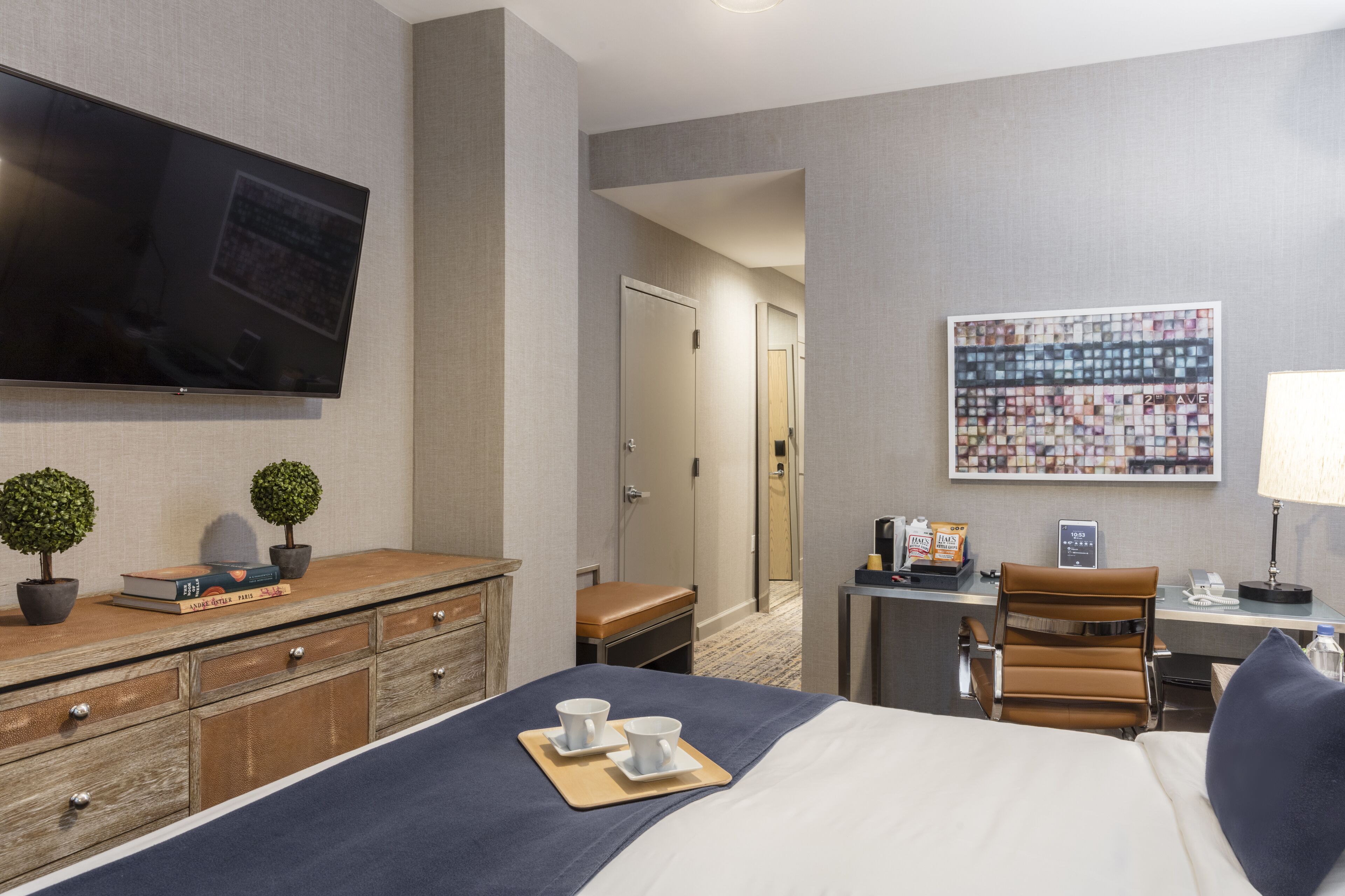 Habitación de hotel con cama, escritorio, televisión, cafetera y un cuadro en la pared.