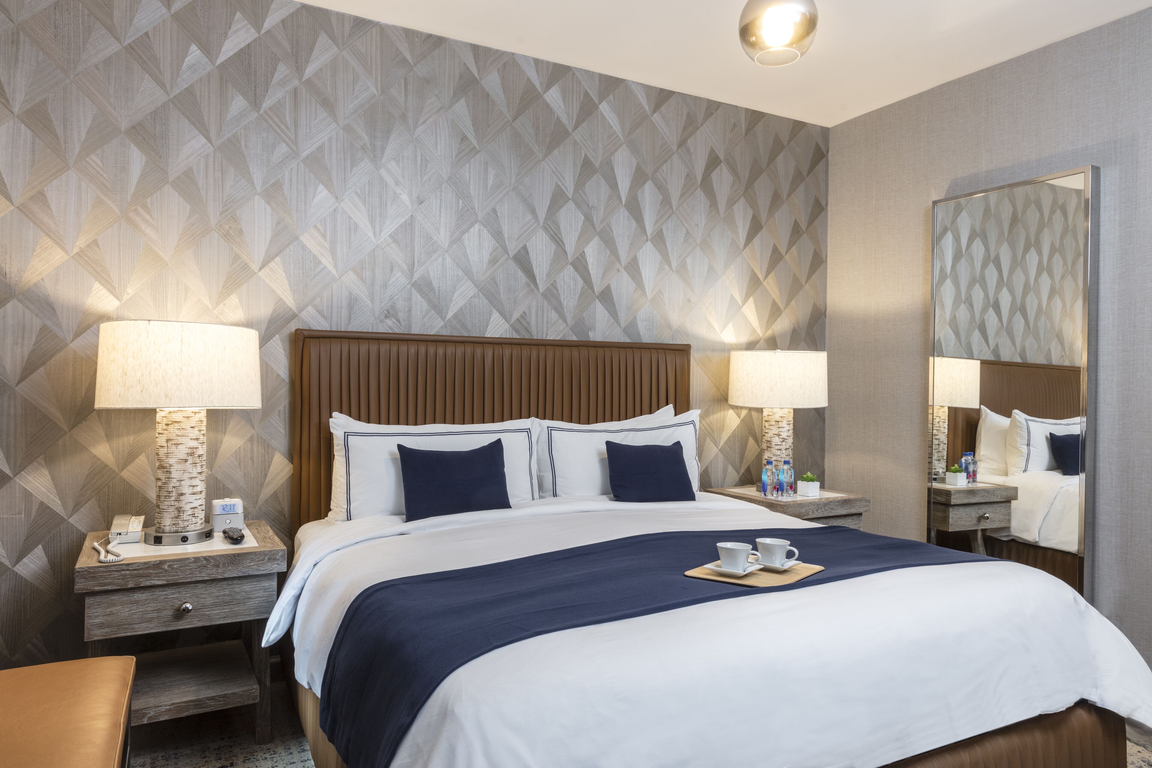 A hotel room with a large bed, two bedside tables, a nightstand, a mirror, and a patterned wall.