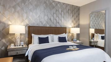 A hotel room with a large bed, two bedside tables, a nightstand, a mirror, and a patterned wall.