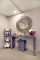 A bathroom with a wooden vanity, a large mirror, a towel rack, and a trash bin.