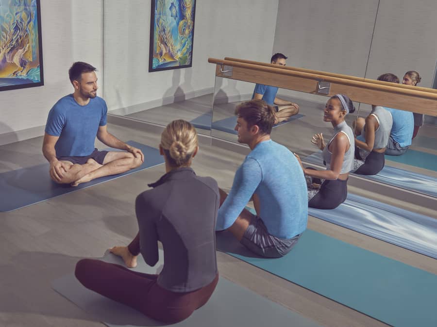 Una clase de yoga en una sala con paredes de espejo y una barra de ballet.