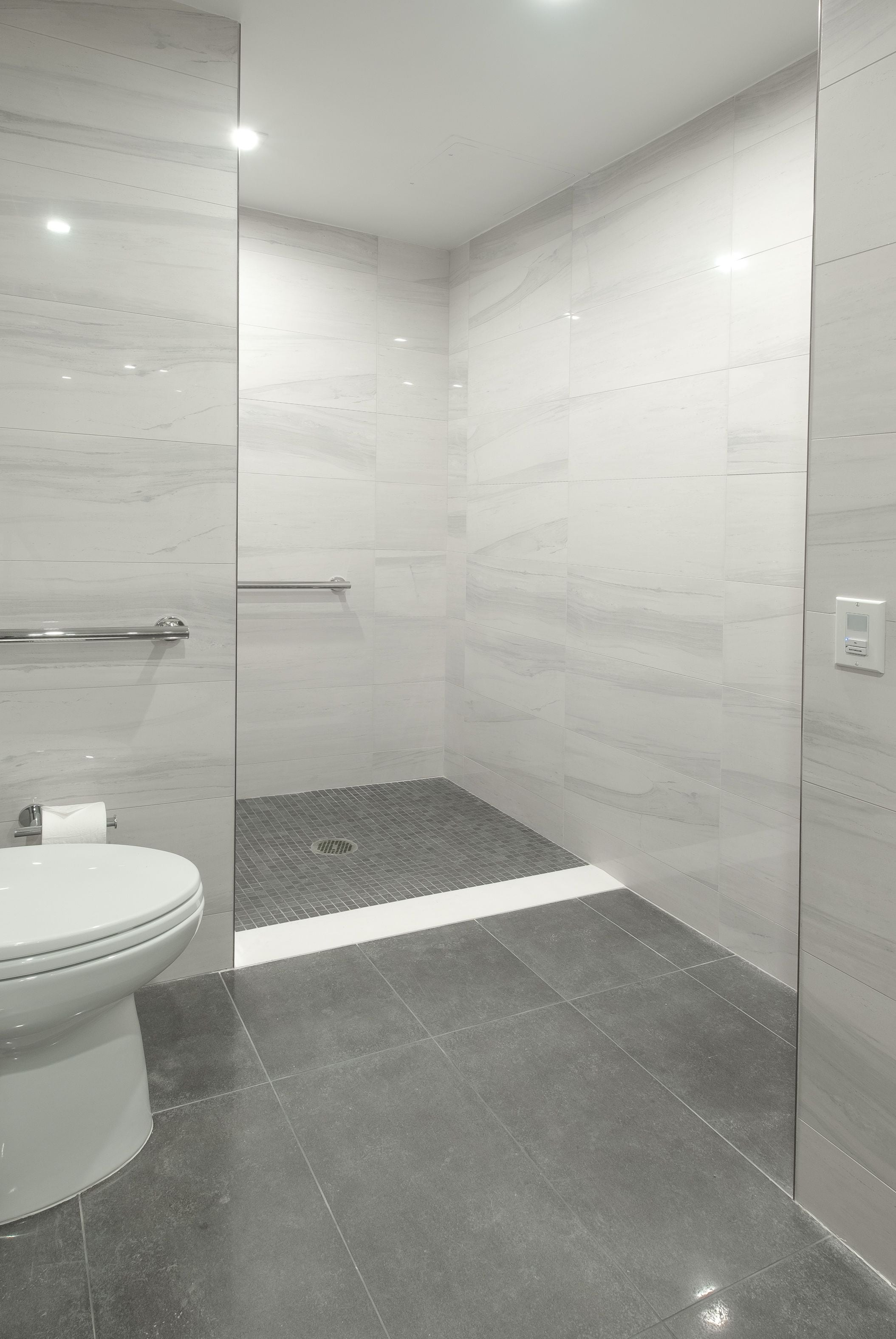 Une salle de bain moderne avec des toilettes, une douche dotée d’une porte en verre et un sol carrelé.