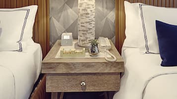 Una habitación de hotel con una cama, una mesita de noche con una lámpara, un reloj y un libro titulado 'Confidential' de Sharon Churcher.