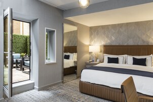 A hotel room with a large bed, a sitting area with a table and chairs, a mirror, and a view of the outdoors.