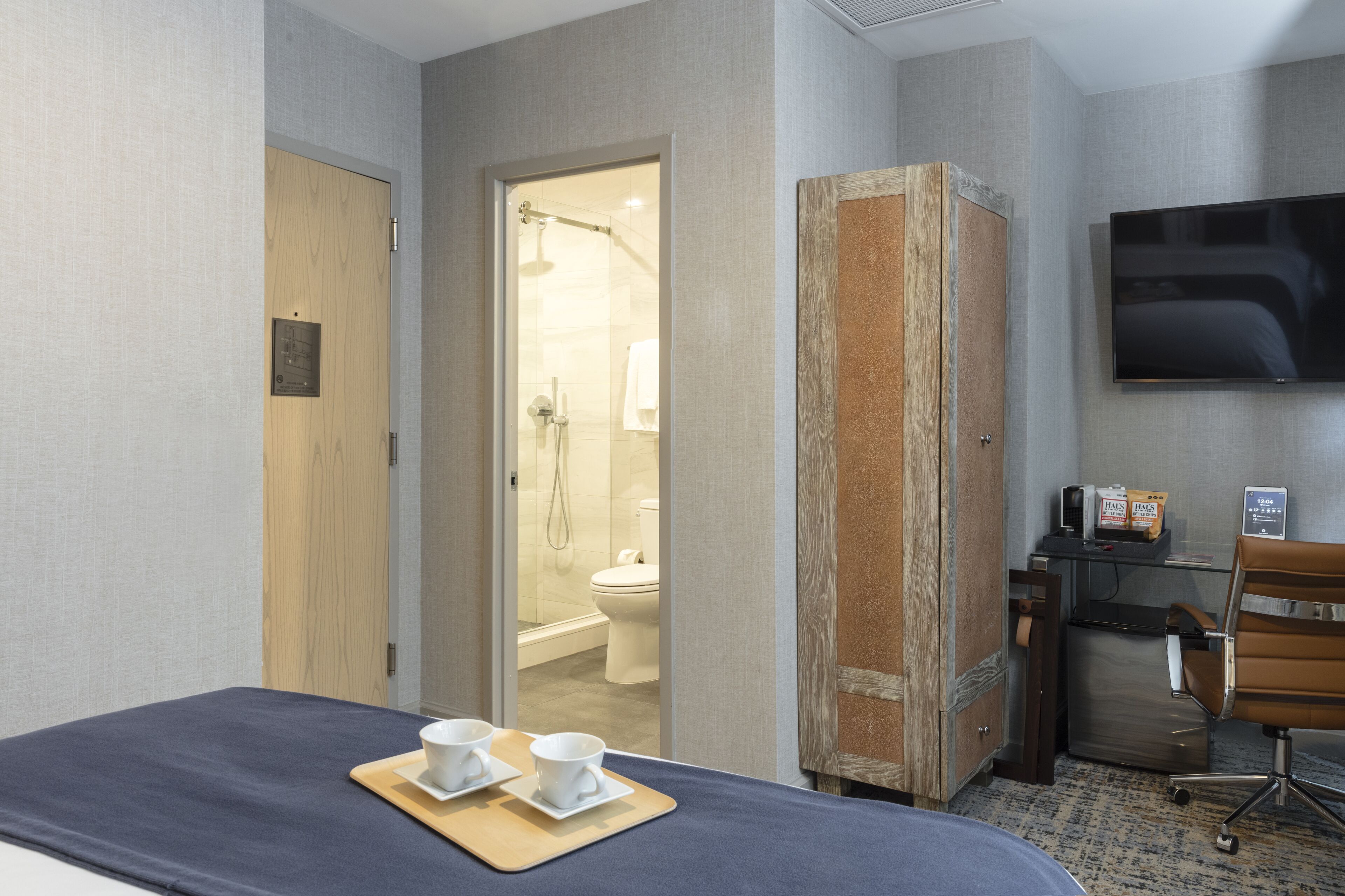Ein Hotelzimmer mit Bett, Schreibtisch mit Stuhl, Fernseher und einem durchgegangenen Tür sichtbaren Badezimmer.