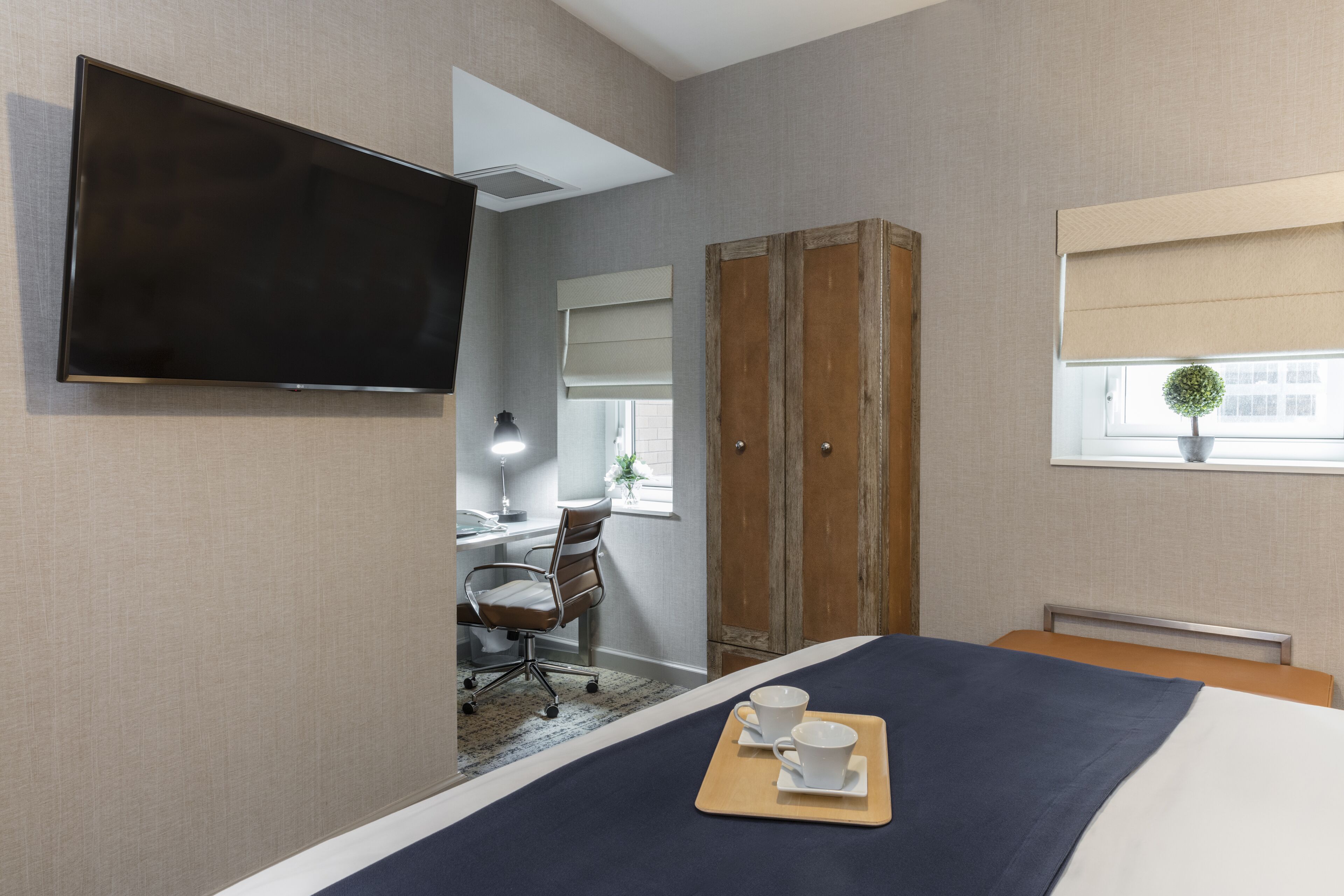 Ein Hotelzimmer mit einem Bett, einem an der Wand montierten Fernseher, einem Schreibtisch mit Stuhl und einem Kleiderschrank.