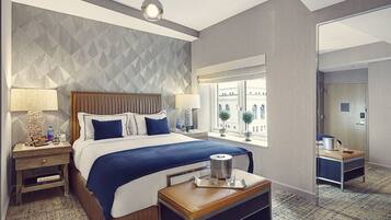 A hotel room with a large bed, two bedside tables, a nightstand, a window with a view, and a small table with a tray.