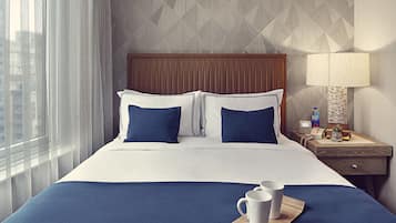 A hotel room with a large bed, a nightstand with a lamp, and a view of the city through the window.