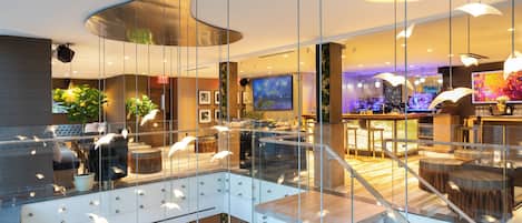 Un vestíbulo moderno de hotel con un atrio de cristal, una zona de bar y diferentes disposiciones de asientos.