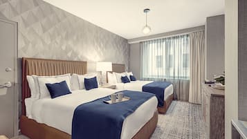 A hotel room with two beds, a desk, and a large window with curtains.
