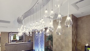 A hotel reception area with a modern design, featuring a curved reception desk, a large digital screen, and multiple hanging pendant lights. - Artezen Hotel (New York)